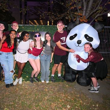 Group of friends posing with a giant inflatable panda at night outdoors.