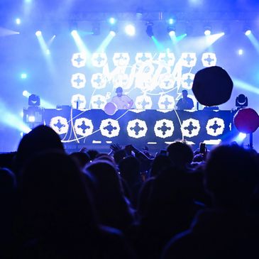 Crowded concert with vibrant blue lights and DJs performing on stage.