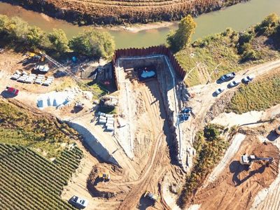 Aerial view of a construction site near a river with heavy machinery and vehicles.