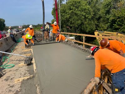 Construction workers pouring and smoothing concrete on a road.