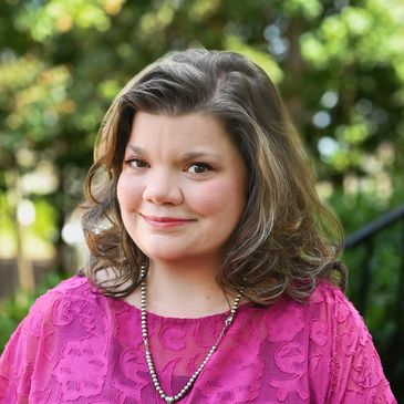 Woman with brown hair wearing a pink top and necklace.