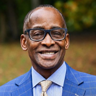 Smiling man in blue suit and glasses outdoors.