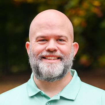 Smiling bald man with a gray beard outdoors.