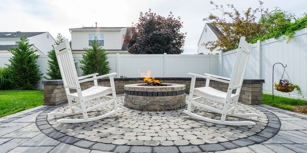 Cozy backyard fire pit with two white rocking chairs and stone patio.