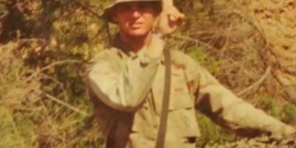 Soldier in camouflage uniform posing in a natural outdoor setting.