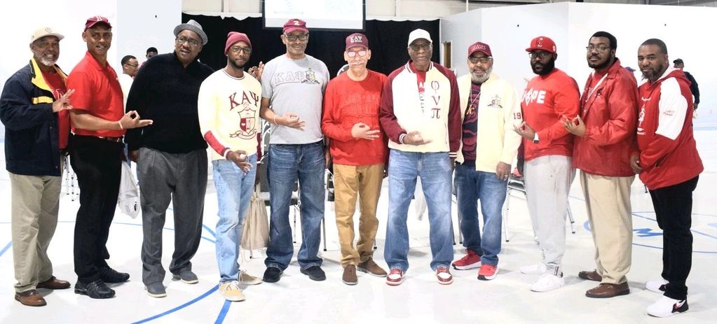A group of men posing together, many wearing fraternity apparel and making hand signs.