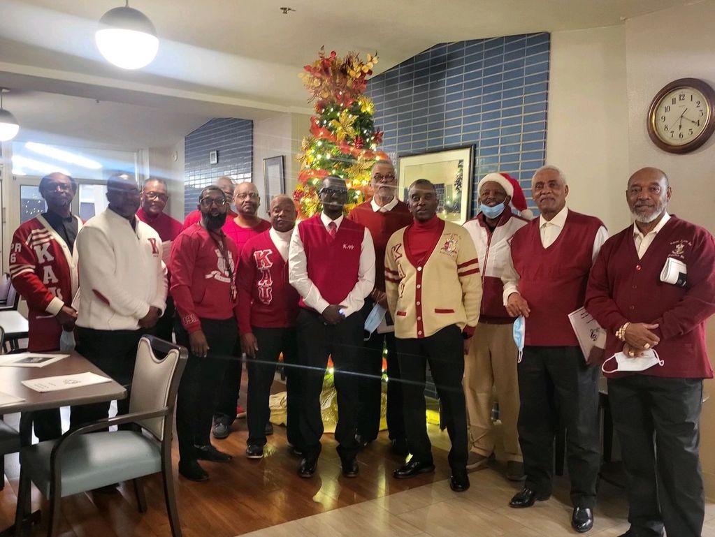 Group of men in festive sweaters posing by a decorated Christmas tree indoors.