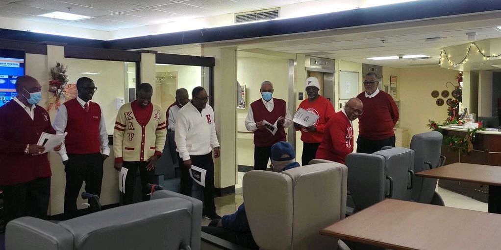 Group of men in red sweaters holding papers in a lounge area.