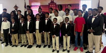 Group of boys in tuxedos posing with adults and two boys in casual clothes indoors.