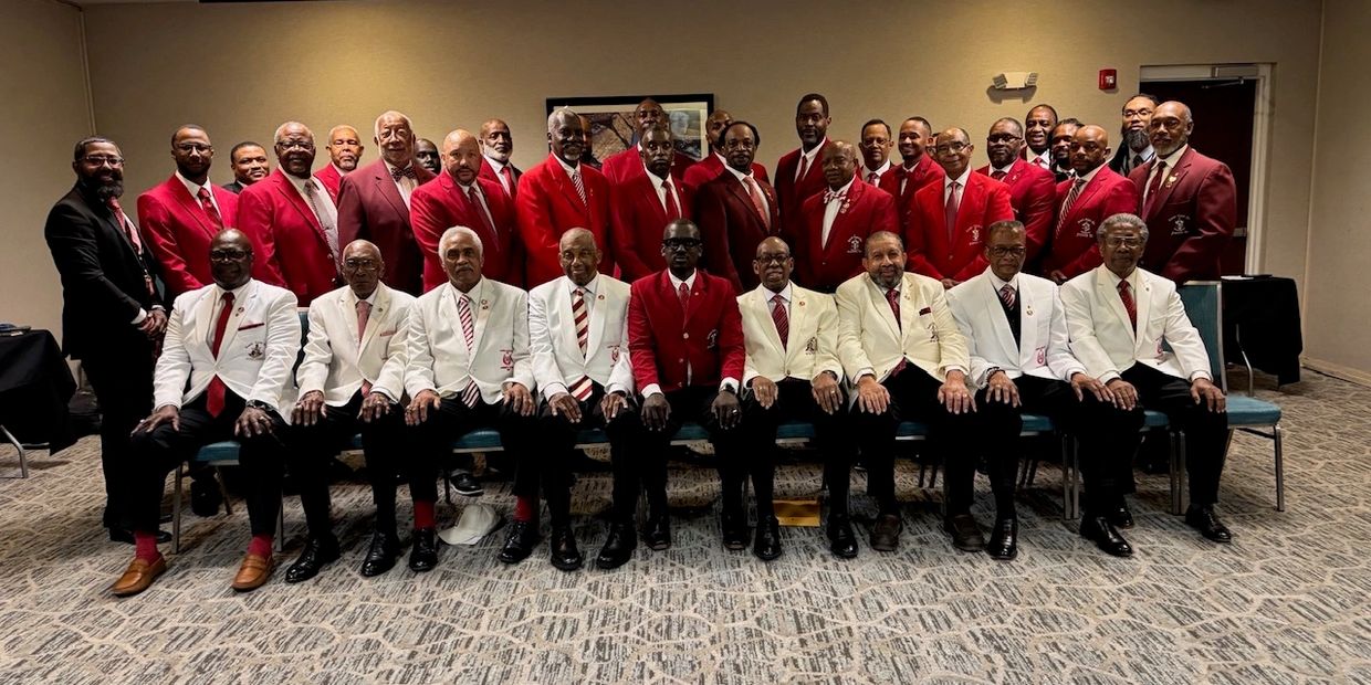 A large group of men in red and white blazers posing for a formal group photo indoors.