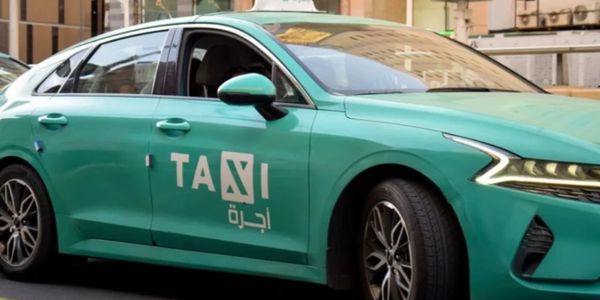 Green taxi car with Arabic and English lettering parked in an urban area.