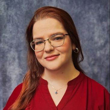Smiling woman with glasses and red hair against a gray backdrop.