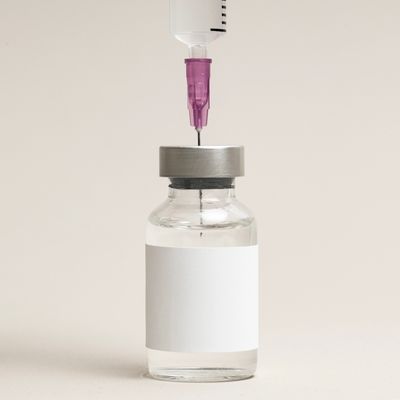 A syringe needle penetrating a vial with a blank label.