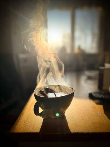 Steaming hot cup of beverage on a wooden table with sunlight.
