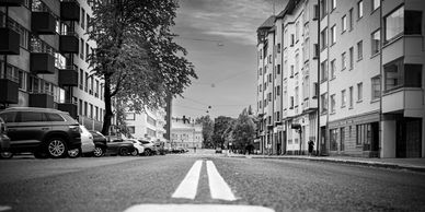 Black and white photo of a city street with buildings and parked cars.