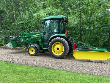 John Deere with a land plane, loader and grapple bucket, on freshly graded gravel driveway.
