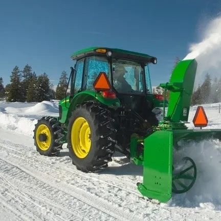 Green tractor clearing snow with a snow blower attachment.