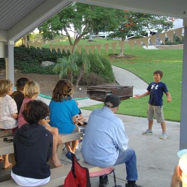 Young boy presenting outdoors to seated audience in a pavilion.