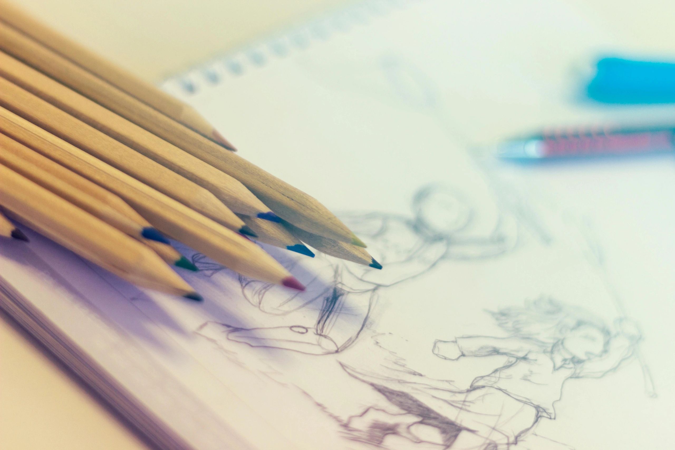Colored pencils resting on a sketchbook with pencil sketches.