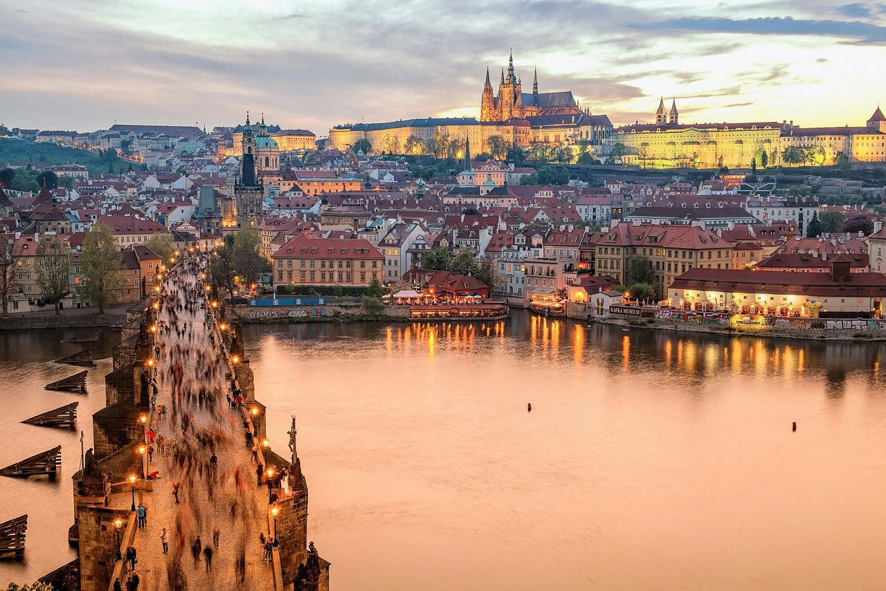 “Autumn evening view of Charles Bridge and Prague Castle glowing above the city.”