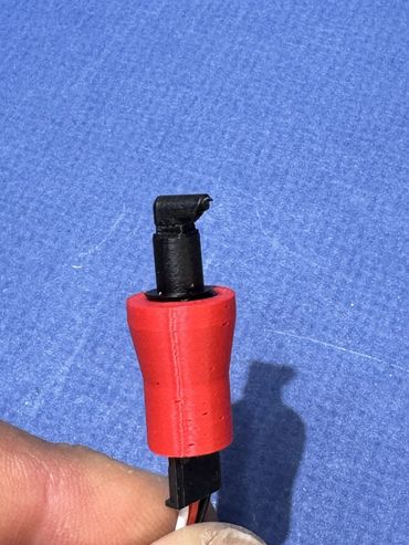 Close-up of a damaged red and black electrical connector held by a hand.