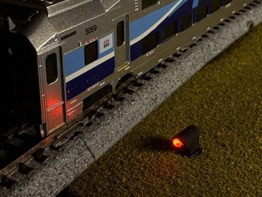 A model train on tracks with a glowing red light signal beside it at night.