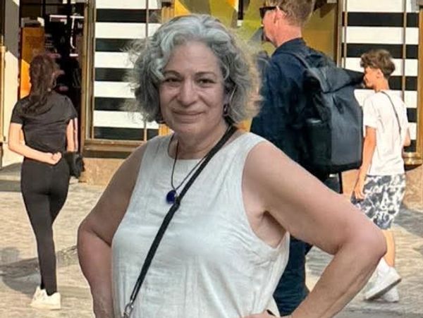 Smiling woman with gray hair wearing a white sleeveless top outdoors.