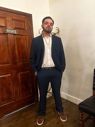 Man in a blue suit standing confidently indoors next to a wooden door.