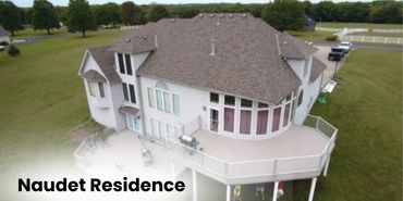 A large, modern house with a spacious elevated deck surrounded by green lawns.