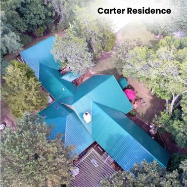 Aerial view of the Carter Residence with turquoise roofs surrounded by trees.
