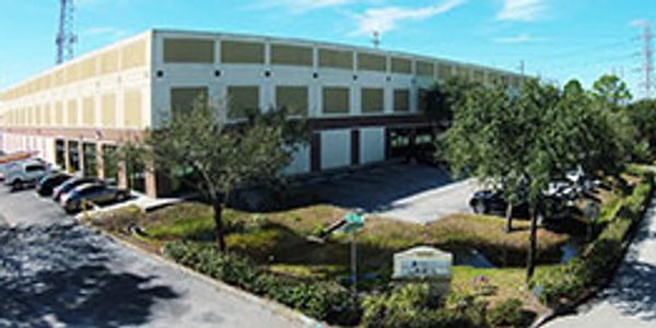 Large warehouse building with parking and greenery under a blue sky.