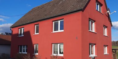 Red two-story house with multiple white-framed windows under a clear blue sky.