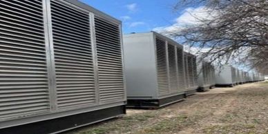 Large industrial air conditioning units lined up outdoors under a clear sky.