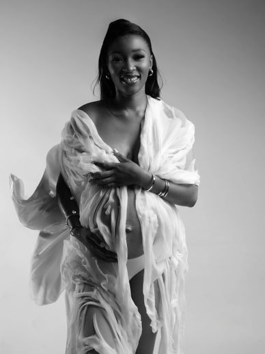 Black and white portrait of a smiling pregnant woman wrapped in flowing fabric.