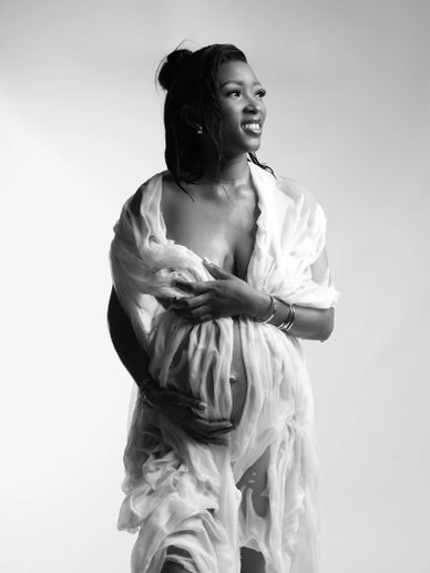 Pregnant woman wrapped in sheer fabric, smiling and looking away.