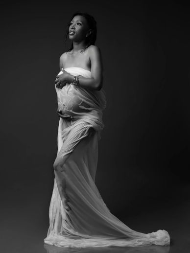 Black and white portrait of a pregnant woman draped in flowing fabric.