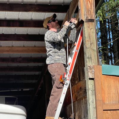 Man on ladder using a power drill on a wooden structure outdoors.