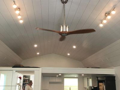 Modern ceiling fan with wooden blades in a well-lit room with vaulted ceiling.