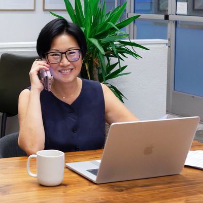 Smiling woman talking on phone at desk with laptop and coffee mug.