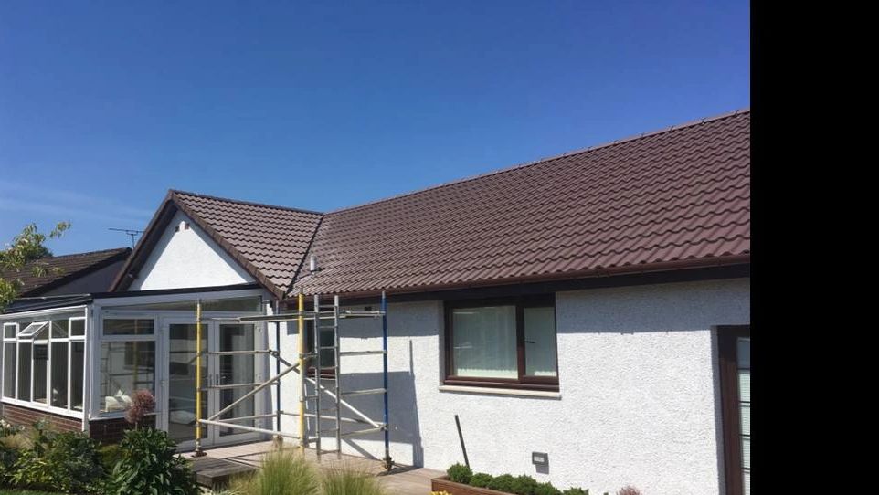 Single-story house with scaffolding and a landscaped garden under a clear blue sky.