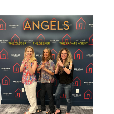 Three women posing as 'Angels' with finger guns against a Red Door Agency backdrop.