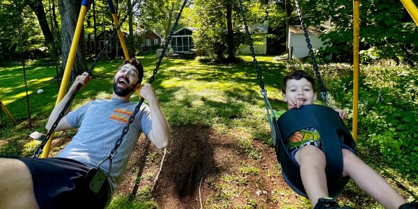 A man and a child joyfully swinging in a sunny backyard.