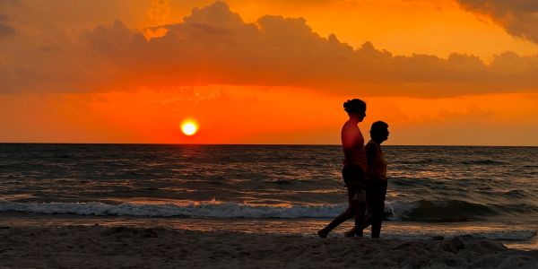 Two people walking on the beach during a vibrant orange sunset.