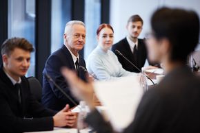 4 people of different ages sitting and looking at a speaker who is blurry in the foreground. 