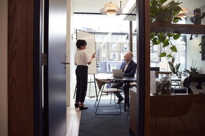 A female-presenting person & a male-presenting person meeting in an office. The female is standing.