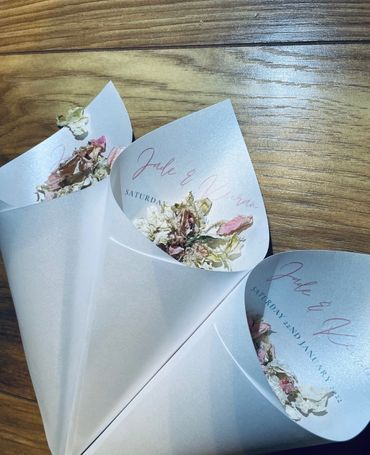 Paper Confetti Cones lay on a wooden table, filled with pink and white, dried, petal confetti.