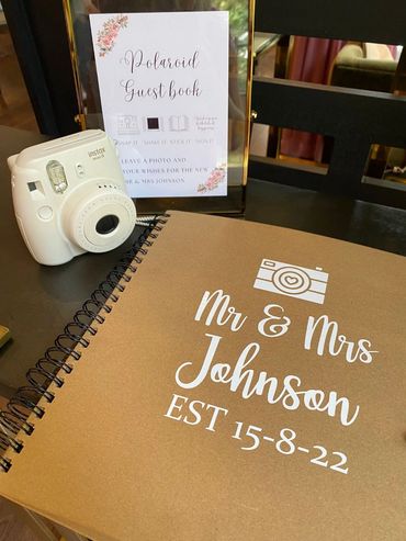 Rustic Brown Wedding Guest Book, with white acrylic wording and a polaroid camera on the table