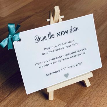 White, Save the Date Invitation with green ribbon bow, sat on a small wooden easel.