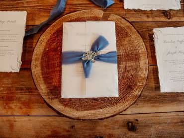 Wedding Invitation with a vellum wrap, a blue ribbon and a grey wax seal, lay on a wooden place mat