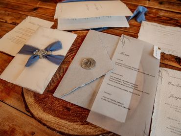 Wedding Invitation set with a vellum wrap, blue ribbons and a grey wax seal, lay on wooden table
